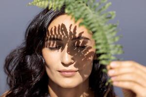 Close-up beauty portrait of a young attractive woman with closed eyes and a green leaf. A beautiful brunette with healthy clear skin and a fern leaf. photo