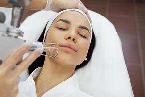 Closeup of the face of young woman undergoing laser resurfacing and peeling procedure in spa salon. photo