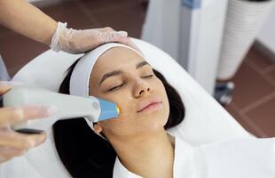 Cosmetologist in grey uniform and transparent gloves makes facial cleansing procedure for her young client photo