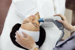 Cosmetologist in grey uniform and transparent gloves makes facial cleansing procedure for her young client photo