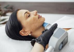 Cosmetician doing laser resurfacing to client in lying on couch in office photo