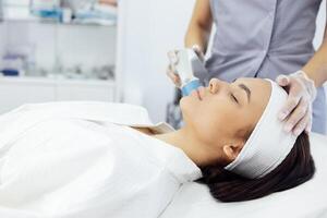 Cosmetologist in grey uniform and transparent gloves makes facial cleansing procedure for her young client photo