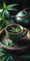 Cup of herbal tea with a cannabis leaf floating on it, surrounded by additional cannabis leaves and buds on a wooden tray photo