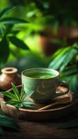 Cup of herbal tea with a cannabis leaf floating on it, surrounded by additional cannabis leaves and buds on a wooden tray photo