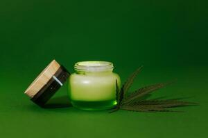 A mock-up of a transparent glass bottle with a cream with moisturizing concentrate, hyaluronic acid and hemp leaves. Facial serum in a jar with peptides and collagen with hemp. photo