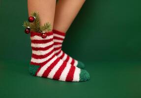 Gils feet in fluffy New Year warm socks. Christmas tree branch with balls decorats female leg. Studio shot. photo