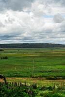 Green fields in the village. Cloudy sky over the fields. Highway in the distance photo