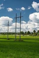 Supports of power lines in a green field. Clouds float across the sky photo