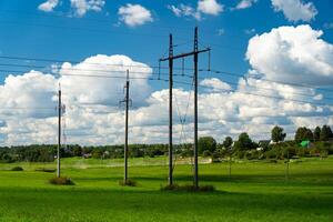 Supports of power lines in a green field. Clouds float across the sky photo