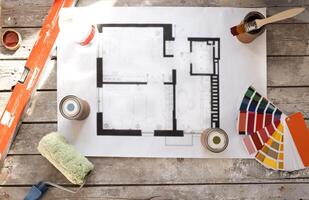 Plan of renovation of house on old wooden table. Top view. Sheet of paper with cans of paint and brushes, palette for choosing colors, construction level and roller. photo