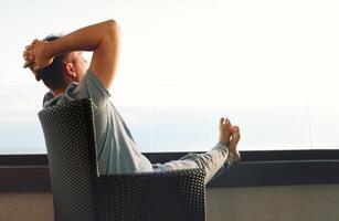 Young man in gray casual clothes sits on wicker chair and put his hands behind his head. photo