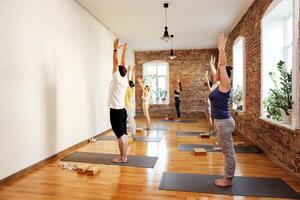 Multiracial smiling people practicing yoga asanas with instructor. Young multiethnic women and men are standing with their hands in up and stretching out. photo