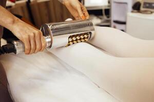 Faceless beautician using massager to remove fat from hips of anonymous customer photo