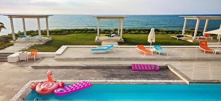Inflatable float rubber objects in the form of a pink mattress and flamingo in the blue water of the pool in sunset photo