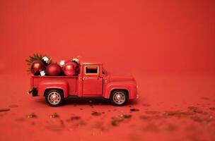 Red toy truck with Christmas balls and fir branch in its trunk. Miniature car with Christmas decoration on red background. Bright backgdrop with sparkles and confetti. photo