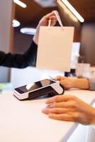 Woman at counter paying with credit card through contactless NFC terminal. The cashier gives the paper bag with the purchase. Shopping in department store. photo
