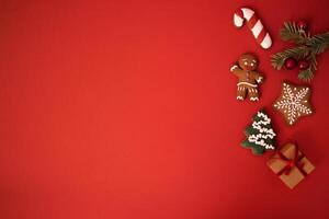 Cute red holiday background with cookies, sprig of fir tree with Christmas balls and a gift in craft paper. Cookies in the form of a gingerbread man, a Christmas tree, stars and a candy cone. photo