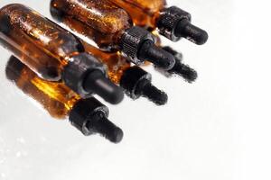 Brown serum or oil glass mock up three bottles with pipette on white background. Group of bottles with drops on them and their reflection on a mirror surface. photo