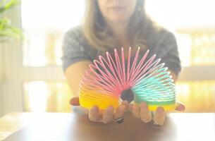 Woman playing with plastic rainbow magic spring to relieve stress while sitting at table at home photo