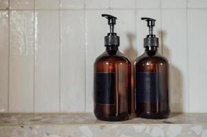 Close-up layouts with brown plastic bottles with dispensers in the bathroom. Mock-ups of shampoo or gel tubes with black empty labels on a background of tiles. photo