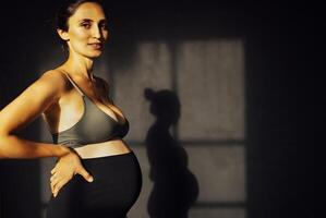 Pregnant woman against a gray texture wall with shadow silhouette photo