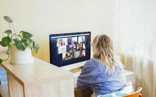 Young woman sits in front of computer monitor and talks via link. photo
