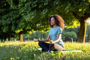 Young woman sitting on grass in park, meditating with closed eyes. Relaxation, mindfulness, and yoga practice in nature. Peaceful and serene outdoor setting. photo