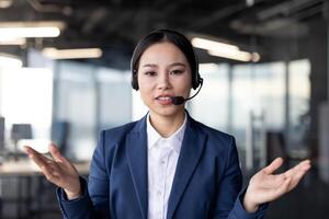 Asian businesswoman using a headset for a call, looking directly at the camera, and talking passionately. Captured in a modern office setting, the image showcases professional communication photo