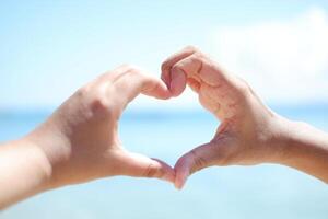 Hands forming a heart shape with the sea in the background. photo