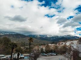 escénico ver de un pequeño pueblo con montañas y nublado cielo en el antecedentes foto