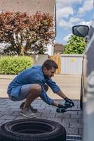 Young man in unscrewing lug nuts on car wheel in process of new tire replacement,using wrench while changing flat tire on the road. photo