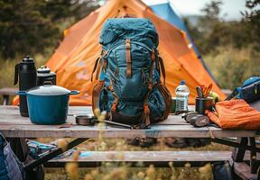 A close up of camping essentials laid out on a picnic table, including a tent, backpack, and cooking gear photo