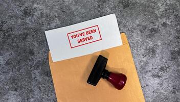 Red Handle Rubber Stamper and You've been served text above brown envelope isolated on wooden background photo