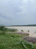 A wide, muddy river stretches across the frame, its waters flowing steadily towards the horizon. photo