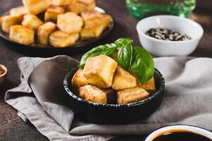 Fried vegetarian tofu cheese cubes and basil leaves in bowl on table photo