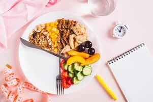 Concept individual meal plan by time food on plate, notebook and alarm clock on table top view photo