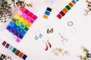 Beautiful beaded earrings, wire, fittings and boxes with colorful beads on the table top view photo