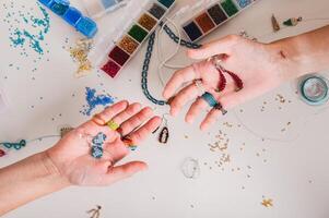 Earrings made of multi-colored beads on the hands of girls above the workplace top view photo