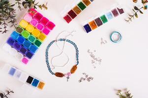 Beaded necklaces, wire, fittings and boxes with colorful beads on a table top view photo