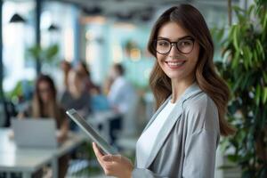 A smiling businesswoman with a tablet computer in her hands standing in the office against the background of working colleagues. photo