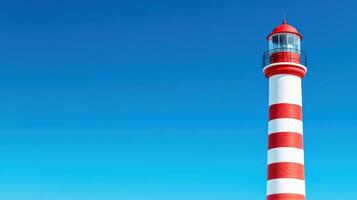 Red and white striped lighthouse against clear blue sky, symbolizing guidance and safety. Ideal for coastal, maritime, and navigational themes. photo