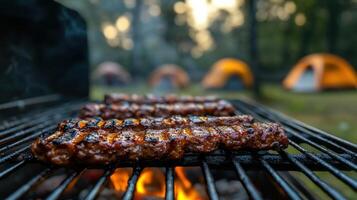 Juicy grilled ribs on a barbecue grill with glowing coals at a campsite with orange tents in the background on a serene forest evening. photo