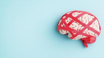 Human brain wrapped in red tape on pale blue background, symbolizing mental health and bureaucratic challenges. photo