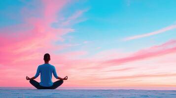 Person meditating in lotus position against a vibrant pink and blue sky during sunset, embracing tranquility and mindfulness. photo