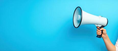A hand holds a megaphone against a blue background, symbolizing communication, announcement, and public speaking. photo