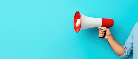 A person holds a megaphone against a bright blue background, illustrating communication, announcements, or promotions. photo