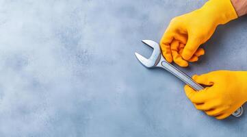 Close-up of hands in yellow gloves holding a wrench on a textured blue background, perfect for maintenance and repair themes. photo