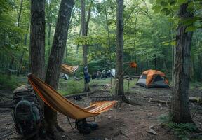 A well organized campsite featuring a hammock strung between trees, a backpack, and a nearby tent photo