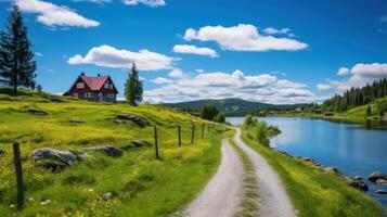 A gravel path winds through a lush green meadow, past a red cottage with a lake and mountains in the background. photo