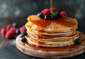 A stack of fluffy pancakes drizzled with maple syrup and topped with fresh berries photo